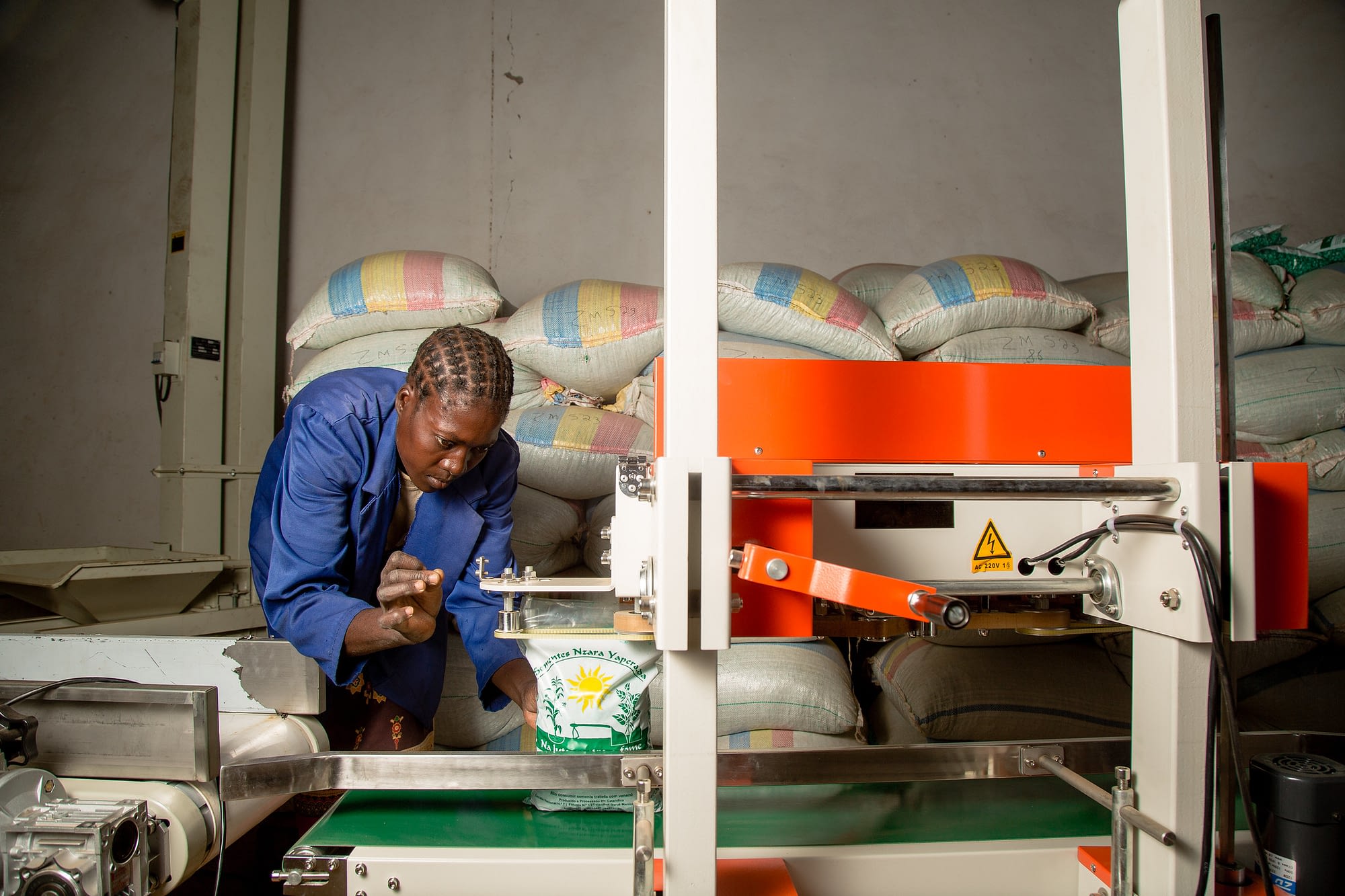 A worker uses a machine to seal a bag of maize seed at the Sementes Nzara Yapera Lda warehouse in Catandika, Mozambique. Photo: CIMMYT/Kipenz Films.